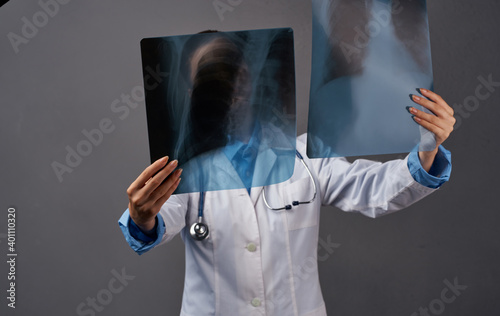 A woman in a medical gown examines X-rays on a gray background