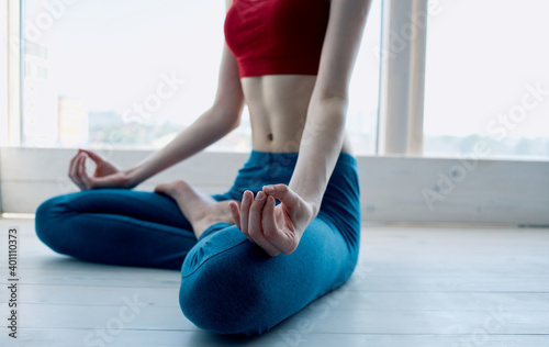 A woman is meditating near the window with her legs crossed and gesturing with her hands