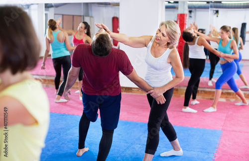 Glad cheerful positive mature woman with her instructor are training self-defence moves in gym.