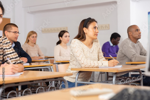 Concentrated hispanic girl attentively listening and making notes of lecture during adult education class