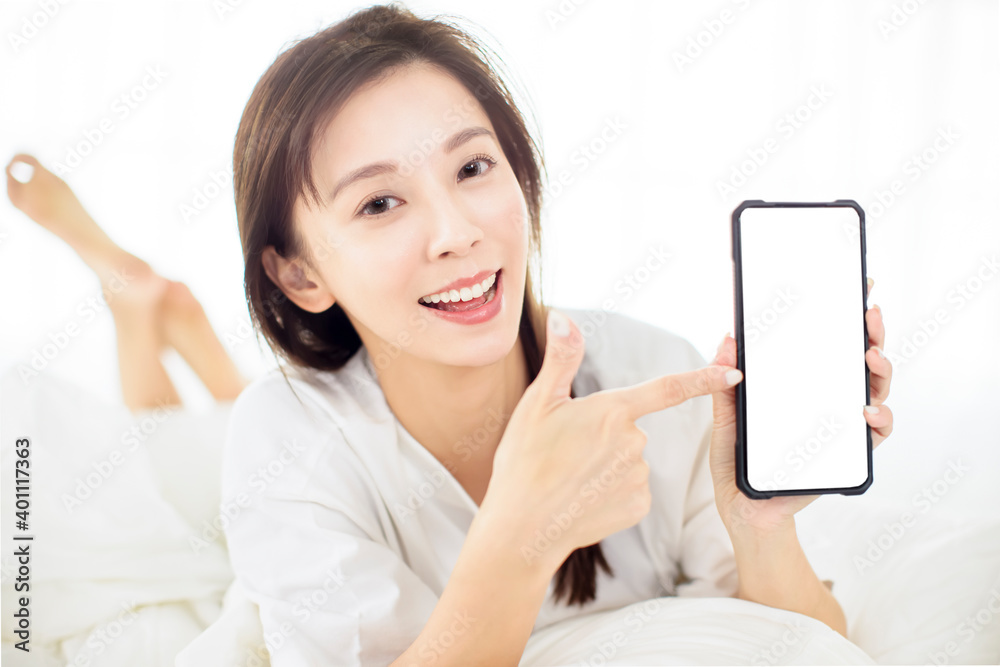 happy young woman showing smart phone while lying on the bed happy young woman showing smart phone while lying on the bed