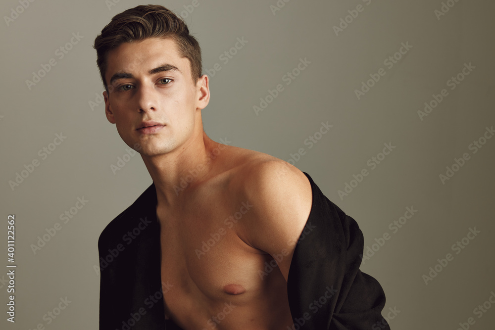 Attractive gentleman with naked shoulders on a beige background with an unbuttoned model jacket Attractive gentleman with naked shoulders on a beige background with an unbuttoned model jacket