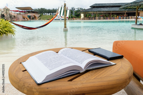 Open book and smartphone on wooden table near the beach of water park. Relaxing concept.