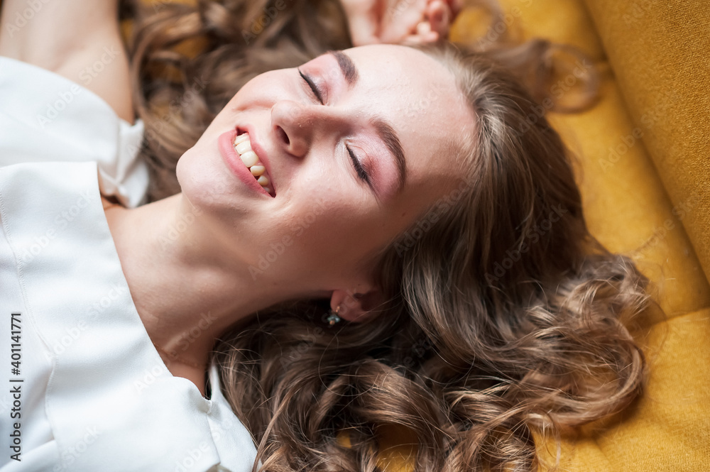 Fototapeta premium A woman is lying on a yellow sofa. Smile with closed eyes.