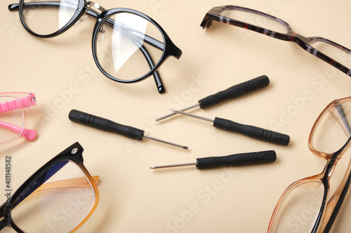 eye glasses and small screwdrivers on beige background, broken glasses, glasses repair concept