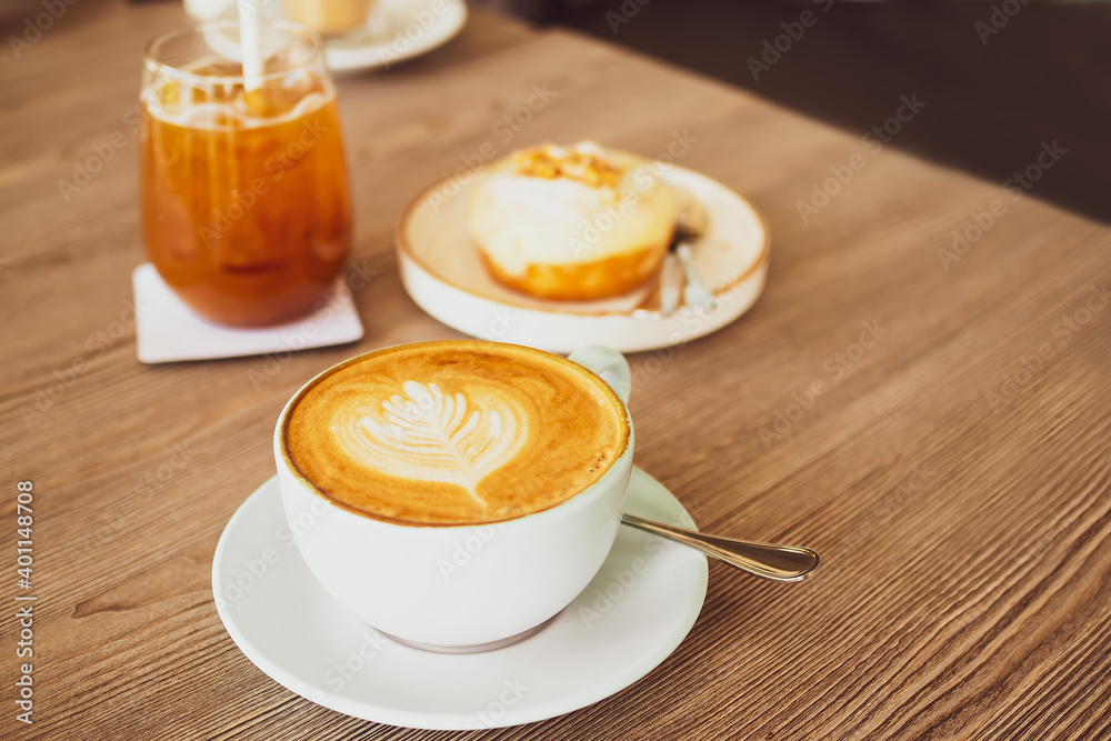 Drink for winter with hot late coffee in white cup and spoon with blur image of tea and cake on wood background. snack fooden. Caffeinated drinks concept. Drink for winter with hot late coffee in white cup and spoon with blur image of tea and cake on wood background. snack fooden. Caffeinated drinks concept.