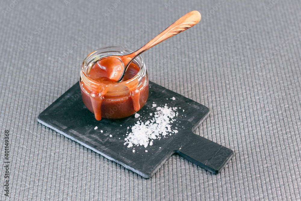 Fototapeta premium Salted caramel in a jar on a gray background on a stone stand. Side view.