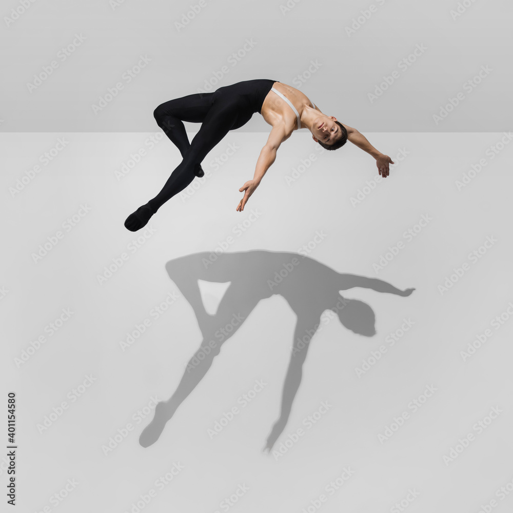 Fototapeta premium Flexible. Stylish young male athlete on white studio background with shadows in jump, air flying. Sportive fit model in motion and action. Body building, healthy lifestyle, style concept.