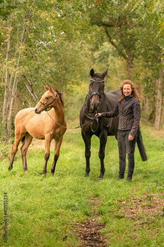 Happy smiling woman next to her horse and foal in the forest. Autumn colors