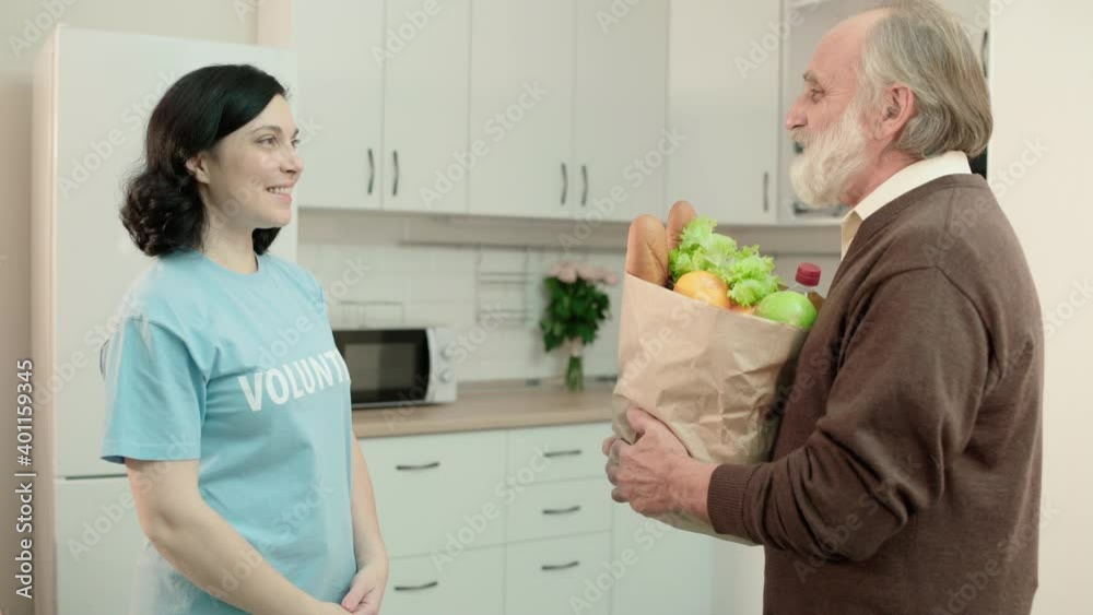 Smiling social worker giving groceries bag to grey-haired senior man, donation Smiling social worker giving groceries bag to grey-haired senior man, donation