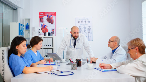 Medical team listening specialist doctor and taking notes during brainstorming sitting in hospital meeting room. Surgeon explaining treatment to coworkers presenting plan during medical conference