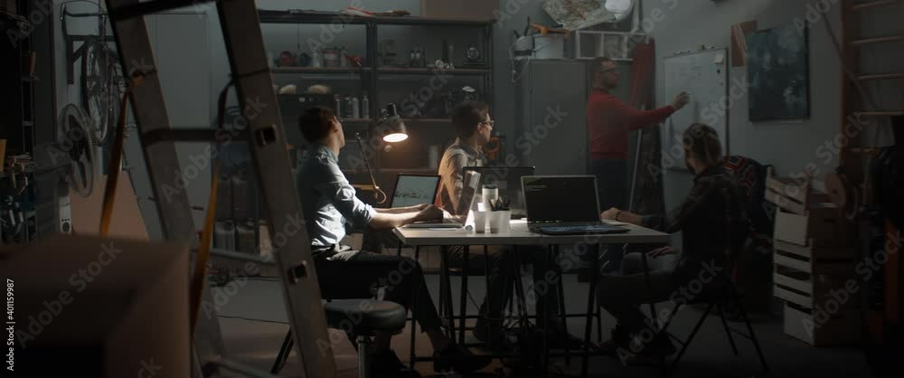 WIDE Group of young people discussing something, brainstorming. Launching their small IT business startup company from garage. Shot with 2x anamorphic lens WIDE Group of young people discussing something, brainstorming. Launching their small IT business startup company from garage. Shot with 2x anamorphic lens