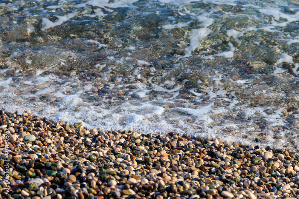 Sea tide on pebble shore of the Mediterranean sea. Waves with white foam on pebble beach Sea tide on pebble shore of the Mediterranean sea. Waves with white foam on pebble beach