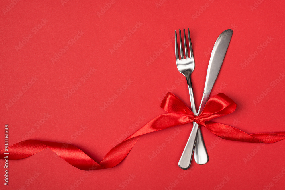 Date in restaurant on valentines day concept. Above overhead close up view photo of silver fork and knife tied with silky red ribbon on vibrant background with empty blank space Date in restaurant on valentines day concept. Above overhead close up view photo of silver fork and knife tied with silky red ribbon on vibrant background with empty blank space