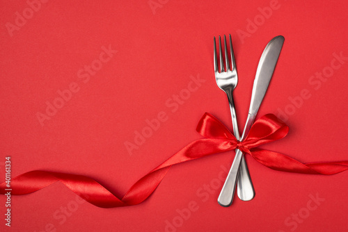 Date in restaurant on valentines day concept. Above overhead close up view photo of silver fork and knife tied with silky red ribbon on vibrant background with empty blank space