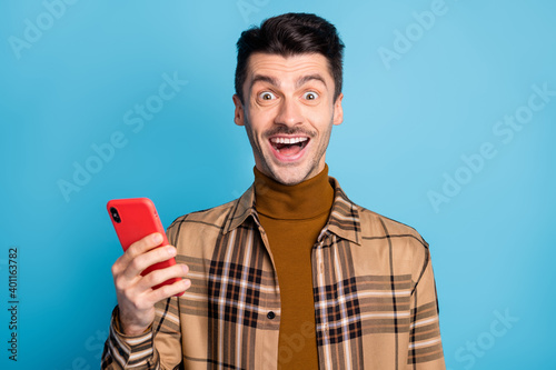 Photo of young happy positive good mood amazed excited man blogger use smartphone isolated on blue color background