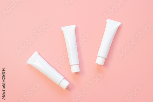 White cosmetic tubes on a pink background. Concept of face and body skin care, cosmetics. Top view, minimalism, flat lay, copy space.