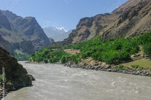 Landscape view of the Afghan side of the Panj river valley in Darvaz district in Gorno-Badakshan, the Pamir mountain region of Tajikistan, with snow-capped mountains in the background