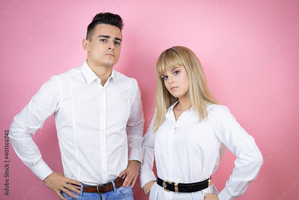 Obraz premium Young couple of girlfriend and boyfriend over isolated pink background skeptic and nervous, disapproving expression on face with arms in waist hugging oneself happy and positive, smiling confident