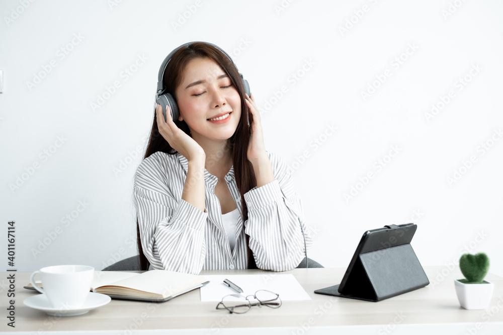 Video Calling a young Asian woman wearing headphones communicates via online long-distance video on a digital tablet happily greetings with a friend Video Calling a young Asian woman wearing headphones communicates via online long-distance video on a digital tablet happily greetings with a friend