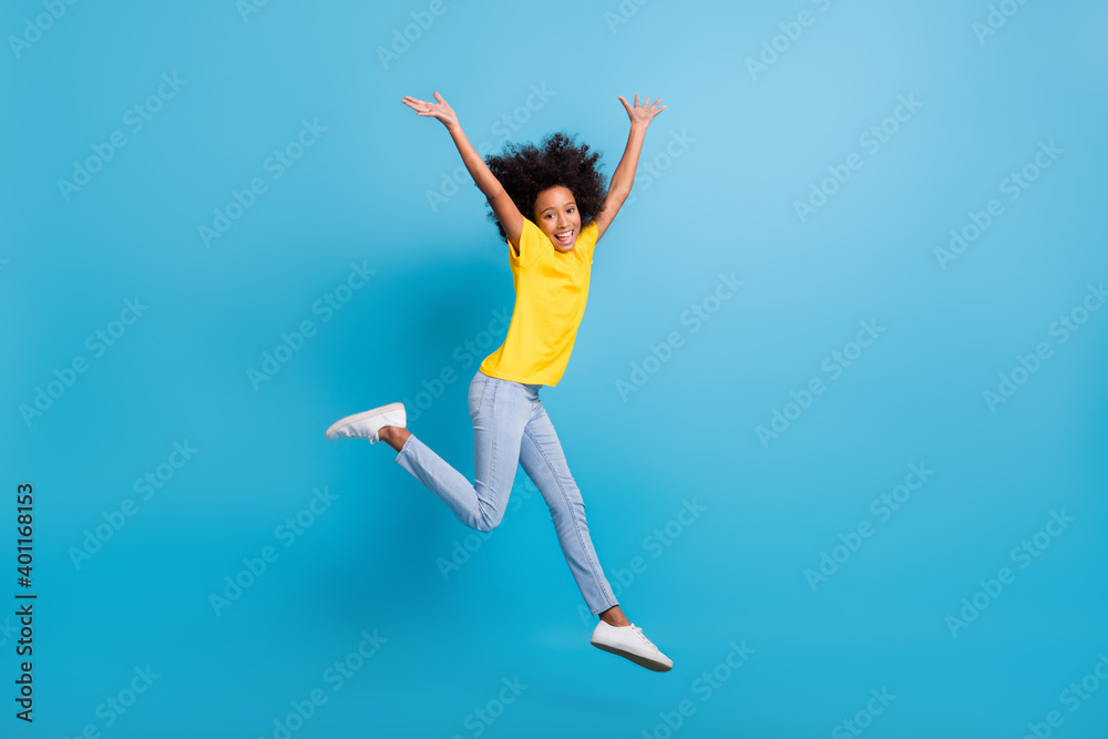 Full body profile side photo afro american volume hair girl wear jeans yellow t-shirt raise hands jump isolated on blue color background