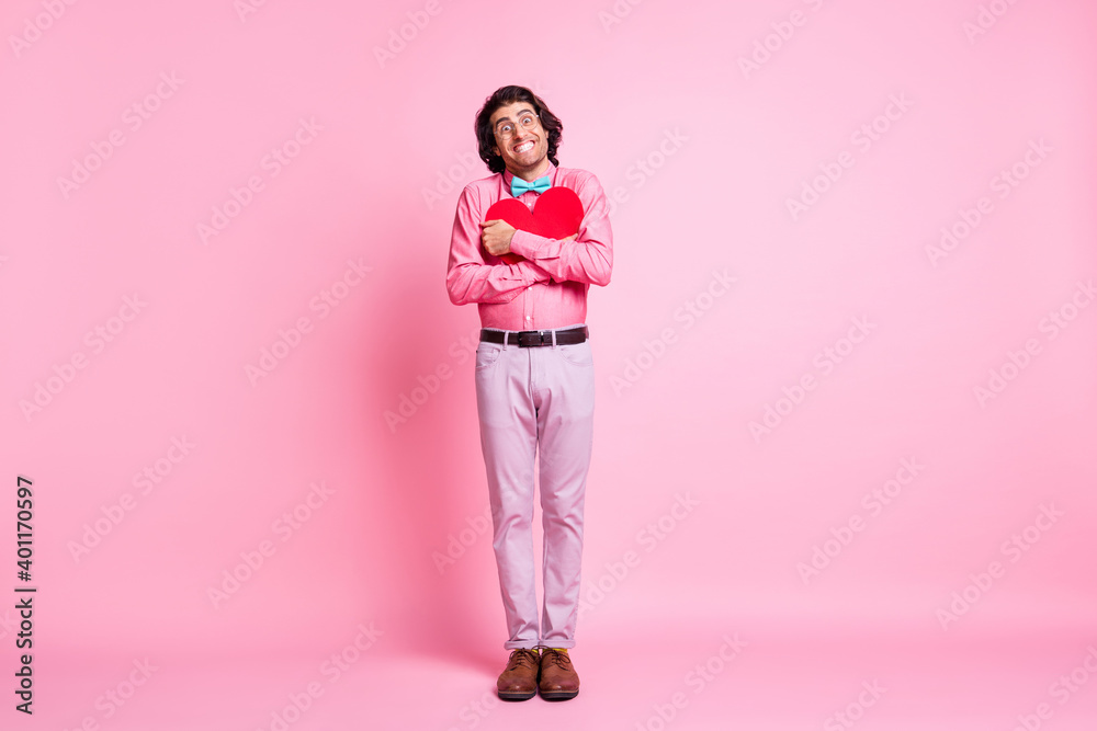 Full length photo of handsome happy guy hug red paper heart beaming smile isolated on pink color background Full length photo of handsome happy guy hug red paper heart beaming smile isolated on pink color background