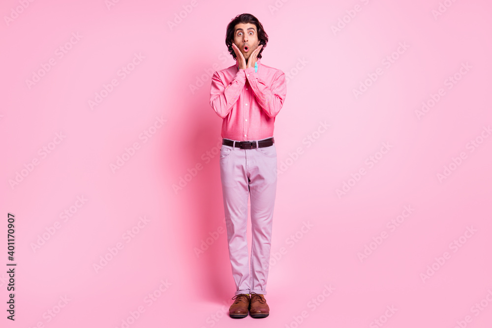 Full size photo of shocked charming young man hold hands cheekbones unexpected present isolated on pink color background Full size photo of shocked charming young man hold hands cheekbones unexpected present isolated on pink color background
