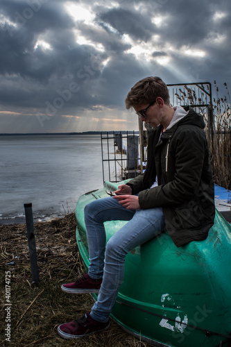 junger Mann sitzt auf Ruderboot während hinter ihm die Wolken brechen