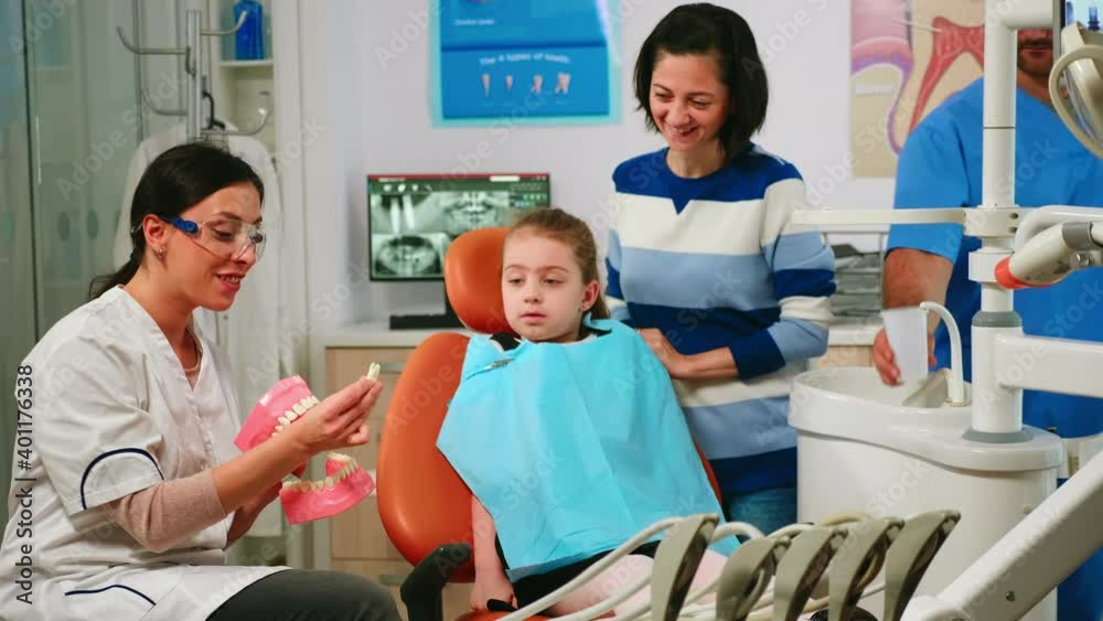 Stomatologist explaining to child the surgery using a plaster model of the mandible extracting a teeth from it. Pediatric dentist holding mock-up of skeleton of teeth, sample of human jaw talking. Stomatologist explaining to child the surgery using a plaster model of the mandible extracting a teeth from it. Pediatric dentist holding mock-up of skeleton of teeth, sample of human jaw talking.