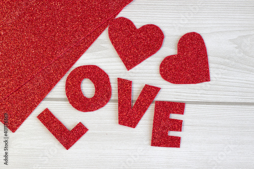 The inscription Love cut out of red glitter paper on a cozy sparkly texture, close up
