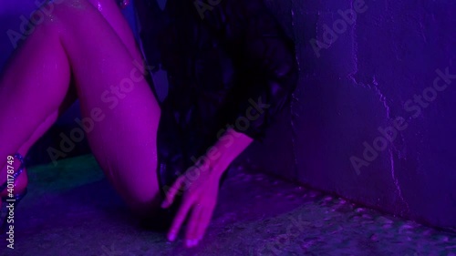 Close-up of a beautiful young wet woman sitting in the shower and posing drenched in water. The view of a young woman in a short black dress and heels. She has sexy legs.