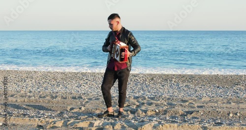 Suonare l'organetto per musica sulla spiaggia in riva al mare da un giovane ragazzo con giacca nera photo