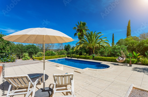 Luxurious pool in the garden of a private villa, hanging chair with pillows for leisure tourists, in summer. Portugal, Algarve.