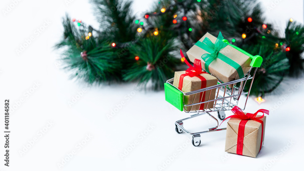 Banner. Small grocery cart with gift boxes on Christmas tree background with garland lights. Creative Christmas shopping online. Holiday sales and discounts for New year. Trading business. Copy space