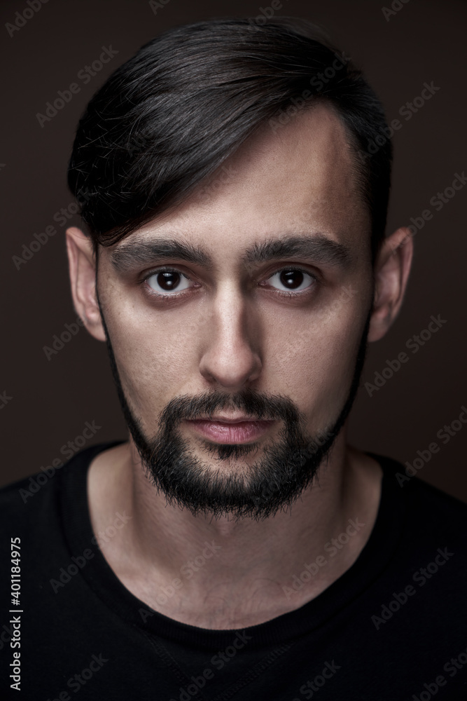 Portrait of handsome caucasian man with beard and stylish haircut in black clothes posing on brown background isolated in studio, fashion model looking at the camera Portrait of handsome caucasian man with beard and stylish haircut in black clothes posing on brown background isolated in studio, fashion model looking at the camera