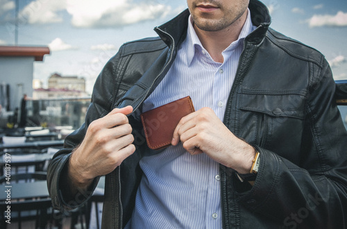 A man in a black leather jacket pulls out a wallet from an inside pocket photo
