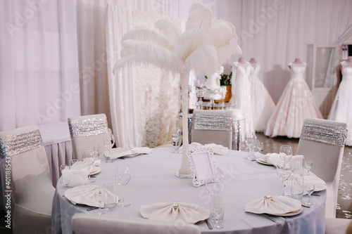 White dinner table decorated with flowers, feathers. Metallic silver wedding decor at luxury style.