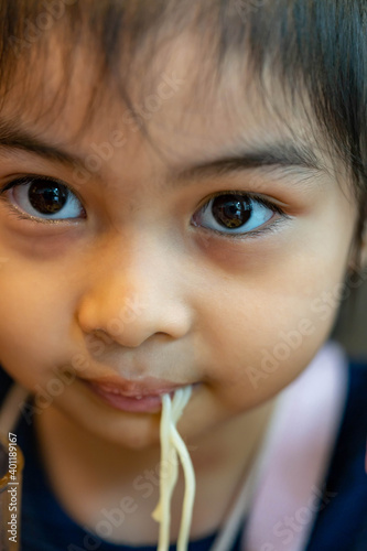 Female asian child while eating noodles. Child eating ramen noodles smiling and enjoying the food. Child eating spaghetti