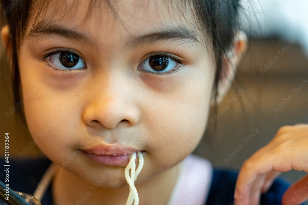 Female asian child while eating noodles. Child eating ramen noodles smiling and enjoying the food. Child eating spaghetti Female asian child while eating noodles. Child eating ramen noodles smiling and enjoying the food. Child eating spaghetti
