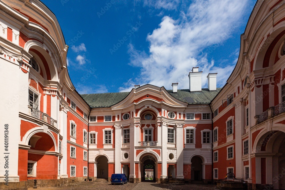 Broumov, Czech Republic - June 17 2020: Courtyard of the famous Benedictine monastery with red and white facade. Sunny summer day with blue sky and white clouds.