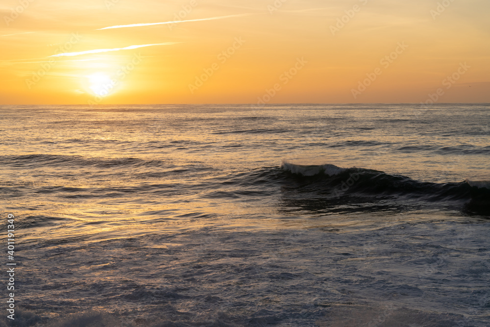 Obraz premium sunset over the ocean with colorful sky and large waves rolling in towards the coast