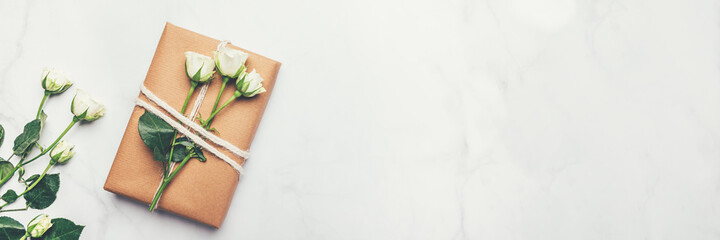 Gift wrapped in recycled brown paper decorated with real fresh roses, on light background with minimalist style wrapping, top view flat lay, eco friendly and zero waste packaging