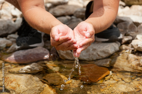 hands grasping cool crystal clear water from a rocky stream on a sunny day. the water falling between the hands