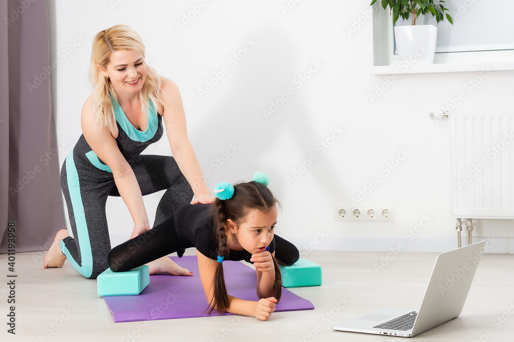 young mother and daughter are engaged in stretching on a laptop online at home during quarantine or lockdown young mother and daughter are engaged in stretching on a laptop online at home during quarantine or lockdown