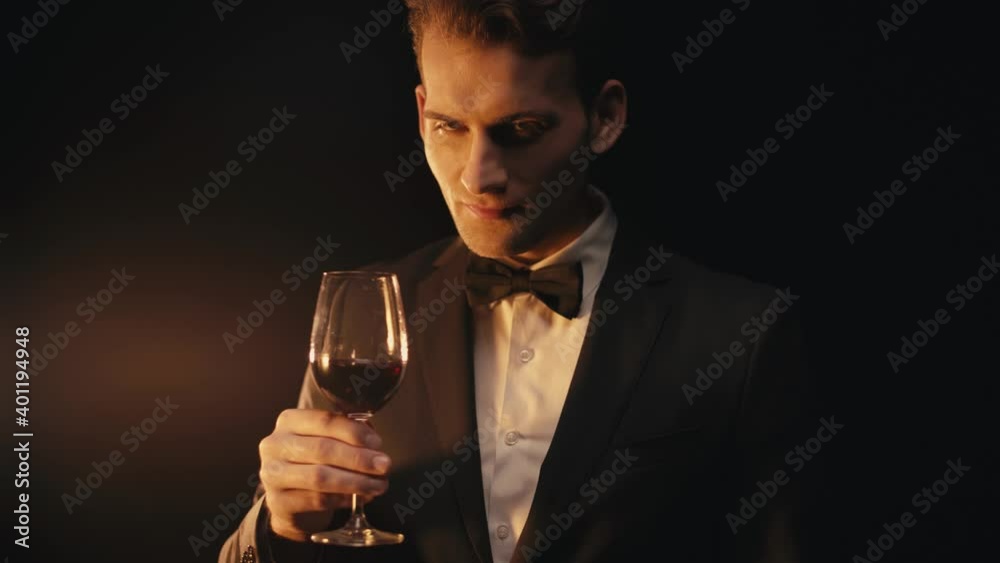 Rack focus of positive man in suit drinking wine on black background