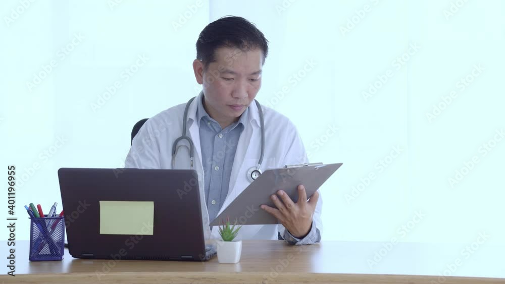 Doctor filling medical history sheet and using laptop at workplace Doctor filling medical history sheet and using laptop at workplace