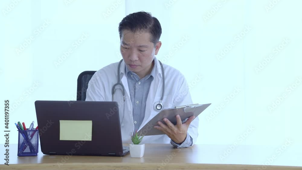 Doctor filling medical history sheet and using laptop at workplace Doctor filling medical history sheet and using laptop at workplace