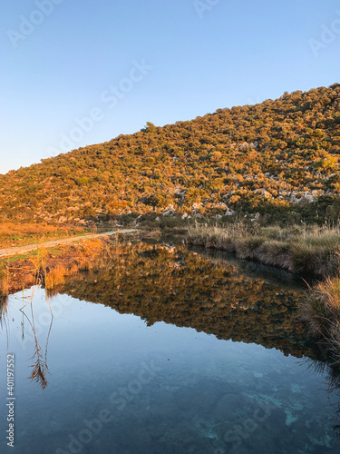 Hills reflection on the surface of the water, pure like a mirror, blue sky background