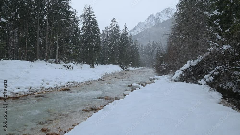 Pristine Alpine river flowing downstream in Slovenia. Snow covering Alps mountains and forest in winter season. Colorful Sava Dolinka river in Alpine valley. Static shot, real time, wide angle Pristine Alpine river flowing downstream in Slovenia. Snow covering Alps mountains and forest in winter season. Colorful Sava Dolinka river in Alpine valley. Static shot, real time, wide angle