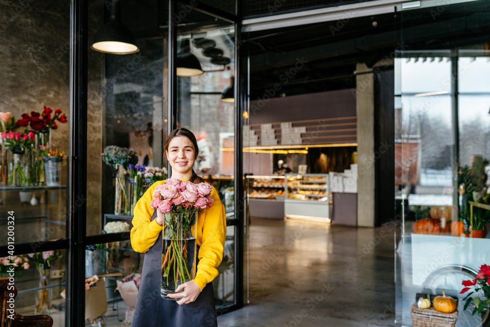Happy smiling busineswoman girl florist holding vase, will do making bouquet of roses in flower shop for customer. Creative occupation in floral boutique. Floristics, business, decoration concept. Happy smiling busineswoman girl florist holding vase, will do making bouquet of roses in flower shop for customer. Creative occupation in floral boutique. Floristics, business, decoration concept.